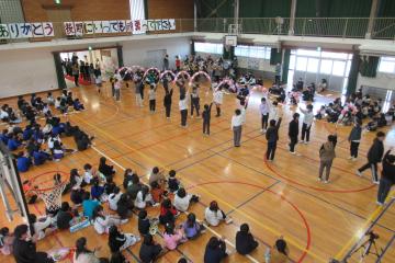 体育館で6年生の児童たちが花アーチを通って入場している様子