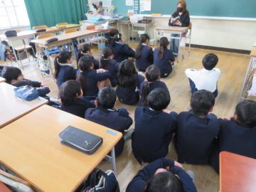 絵本の読み聞かせを教室の床に座ってたのしむ4年生