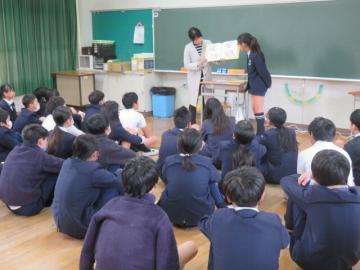 英語絵本の読み聞かせを教室の床に座ってたのしむ6年生