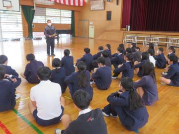 体育館に座る生徒と、その前に立って話をする男性教師