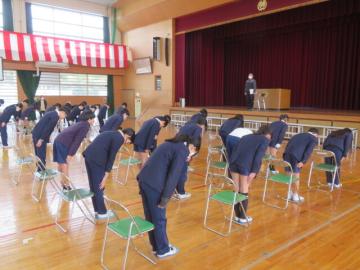 体育館に並んだパイプ椅子の前でお辞儀をする生徒たち