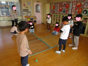 室内の床でコマ回しをする園児たちの様子