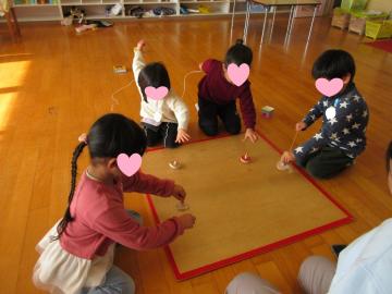 室内の床で糸引きゴマで遊ぶ園児たちの様子