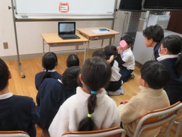 教室でオンラインの絵本読み聞かせをパソコンの前に座って見る児童たちの様子