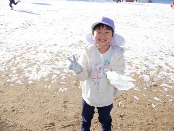 集めた雪をもつ幼児が庭でピースサインをするようす