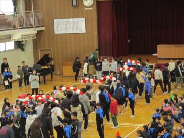 体育館で1年生が花のアーチで6年生の入場を迎えているところ