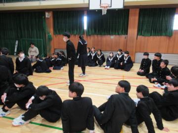 借り人競争　1クラス分の生徒たちが体育館で輪になって座る中心に生徒が立っている様子