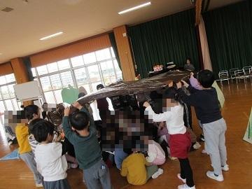 遊戯室で全園児がオオカミのお腹の大きなポリ袋の中に隠れている写真