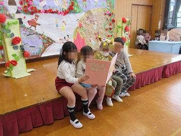 遊戯室のステージの段差に腰掛けて大きな本を読む園児たち