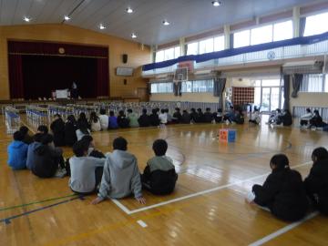 体育館で6年生が輪になって床に座って開会するようす