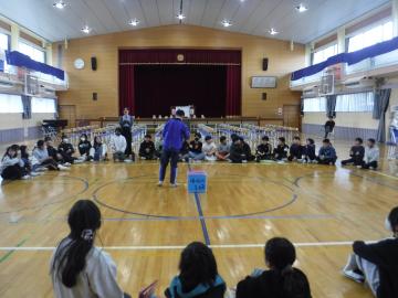 体育館で座った生徒の輪の中央でトークする生徒のようす