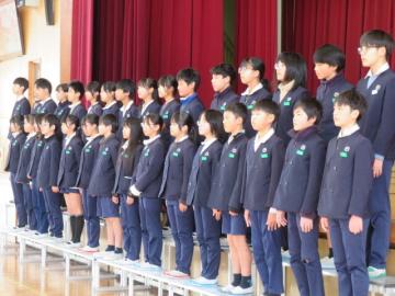 体育館の壇上のひな壇で整列している6年生