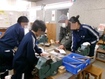 技術室で先生に教えてもらいながら機械を使って作業する生徒たち