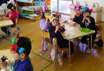 椅子に座った園児が恵方巻を食べているところ
