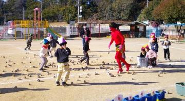 庭で園児が赤鬼にマメを投げているところ