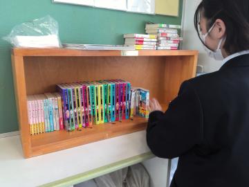 図書部の生徒が、教室で学級文庫を本棚に並べているようす