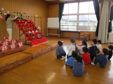 ひな人形を指しながら話をする教師とそれを見ながら座って聞く子供たち