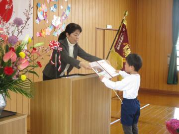 遊戯室のステージで園長から修了証書を受け取る子供