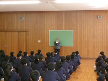 第2体育館の武道場で、2組の担任が整列している生徒の前でお話をしています。