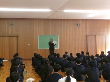 第2体育館の武道場で、1組の担任が整列している生徒の前でお話をしています。