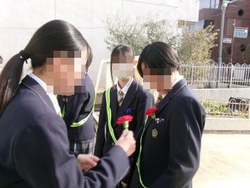 生徒会役員が校門で登校した3年生にコサージュを付けています1