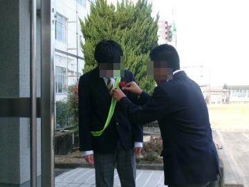 生徒会役員が校門で登校した3年生にコサージュを付けています2