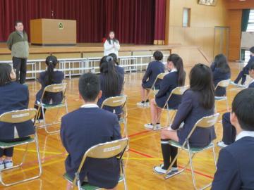 体育館で1年時担任からのお祝いのことばを聞く6年生の様子