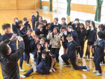体育館で元担任を囲んで記念写真を撮る6年生の様子