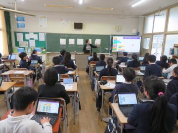座席に座って話を聞く5年生に電子黒板のモニターを使ってプログラムのアレンジを説明する校長