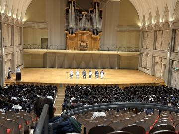 パルナソスホールのステージに立つ数名の生徒と、客席で座っている生徒たち