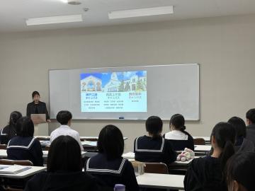 会議室でスクリーンに資料を映しながら説明する講師と、椅子に座って話を聞く生徒達2