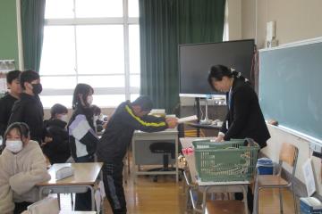 担任の先生が教室で児童たちに順番に通知表を手渡している様子