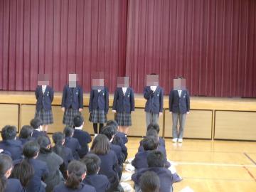 体育館の壇上に整列し、クラスの代表生徒が話している様子