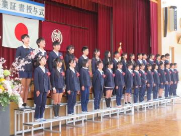 体育館でひな壇に立ち旅立ちの日にを歌う6年生