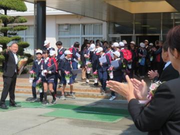 校舎の玄関で先生方からバラの花を受け取る6年生