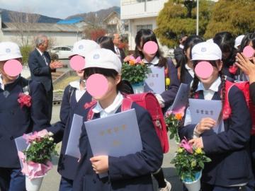 屋外で卒業証書と花を手に花道へと進む6年生