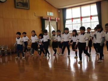 遊戯室で横一列に並んだ子供たちが同じ方向に歩いている園児たちの様子