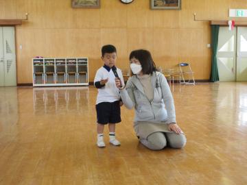遊戯室で司会をする子供とその子供にマイクを向ける教員の様子
