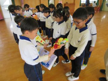 遊戯室で立って向き合う子供たちがプレゼントを渡し合う園児たちの様子