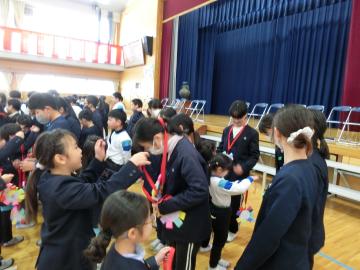 体育館で1年生が6年生にメダルを渡しているところ