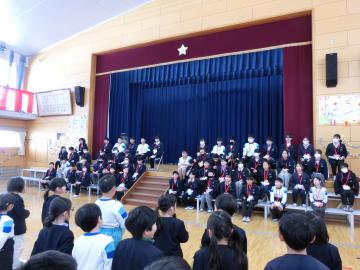 1年生が体育館のステージに座る6年生にメッセージを述べているところ