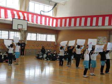 体育館で2年生が画用紙を頭の上に掲げている様子