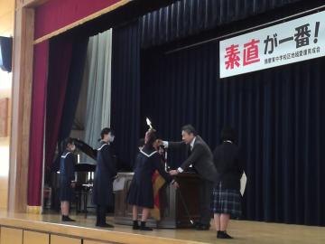 女子テニス部の生徒が、体育館の壇上で優勝旗を受け取る様子