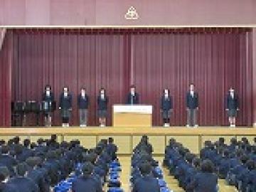 体育館の壇上に整列し、新生徒会長が着任の挨拶をする様子