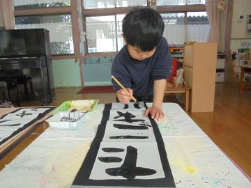年長児が書初めでたこあげの文字をかいている