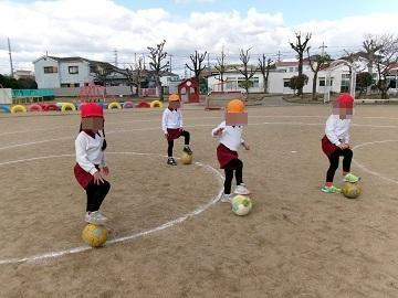 運動場でボールに片足をのせて立っている子供たちの写真