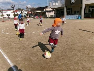 運動場でサッカーボールの上をジャンプしている子供たち
