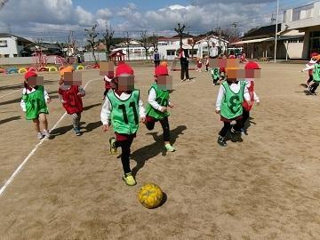 運動場でサッカーの試合をして、ボールを追いかける園児たち