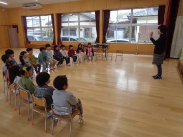 園児が遊戯室に集まって園長先生からひなまつりについての話を聞いている