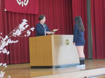 5年生を代表して体育館のステージで校長から修了証を受け取る児童